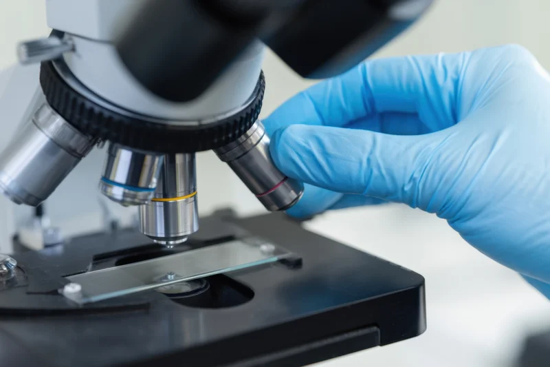 Scientist adjusting microscope objective over glass slide in laboratory