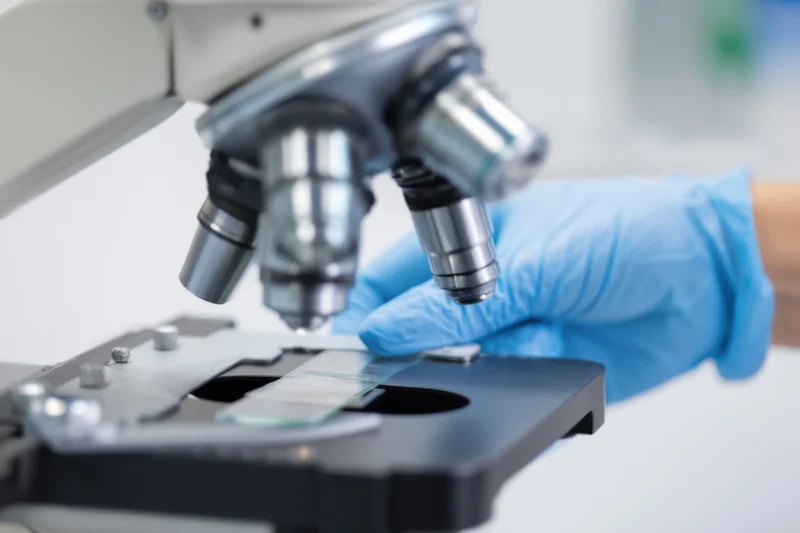 Scientist placing a glass slide under a microscope in a laboratory setting
