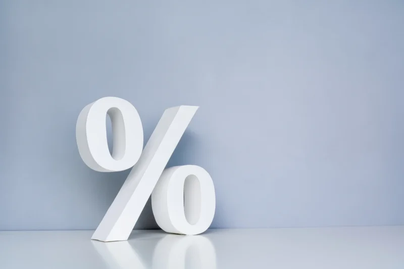 Large white percentage symbol standing on a reflective surface against a light blue background