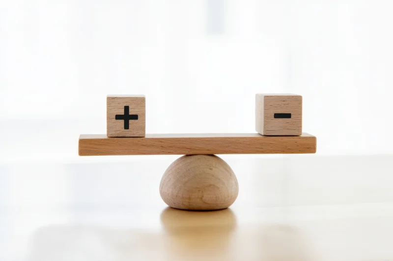 Wooden balance scale with plus and minus cubes on white background