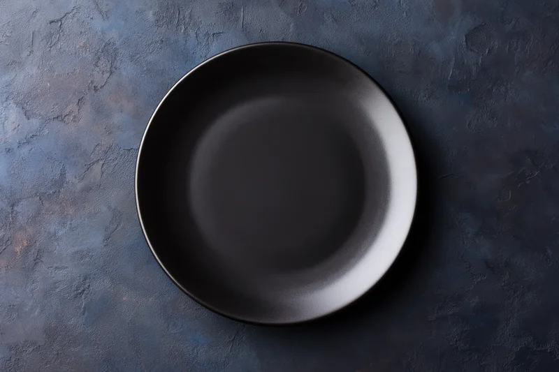 Black ceramic plate centered on dark textured surface with copyspace for text or design