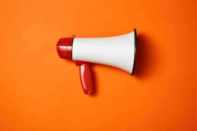 Red and white plastic megaphone lying flat on vibrant orange background