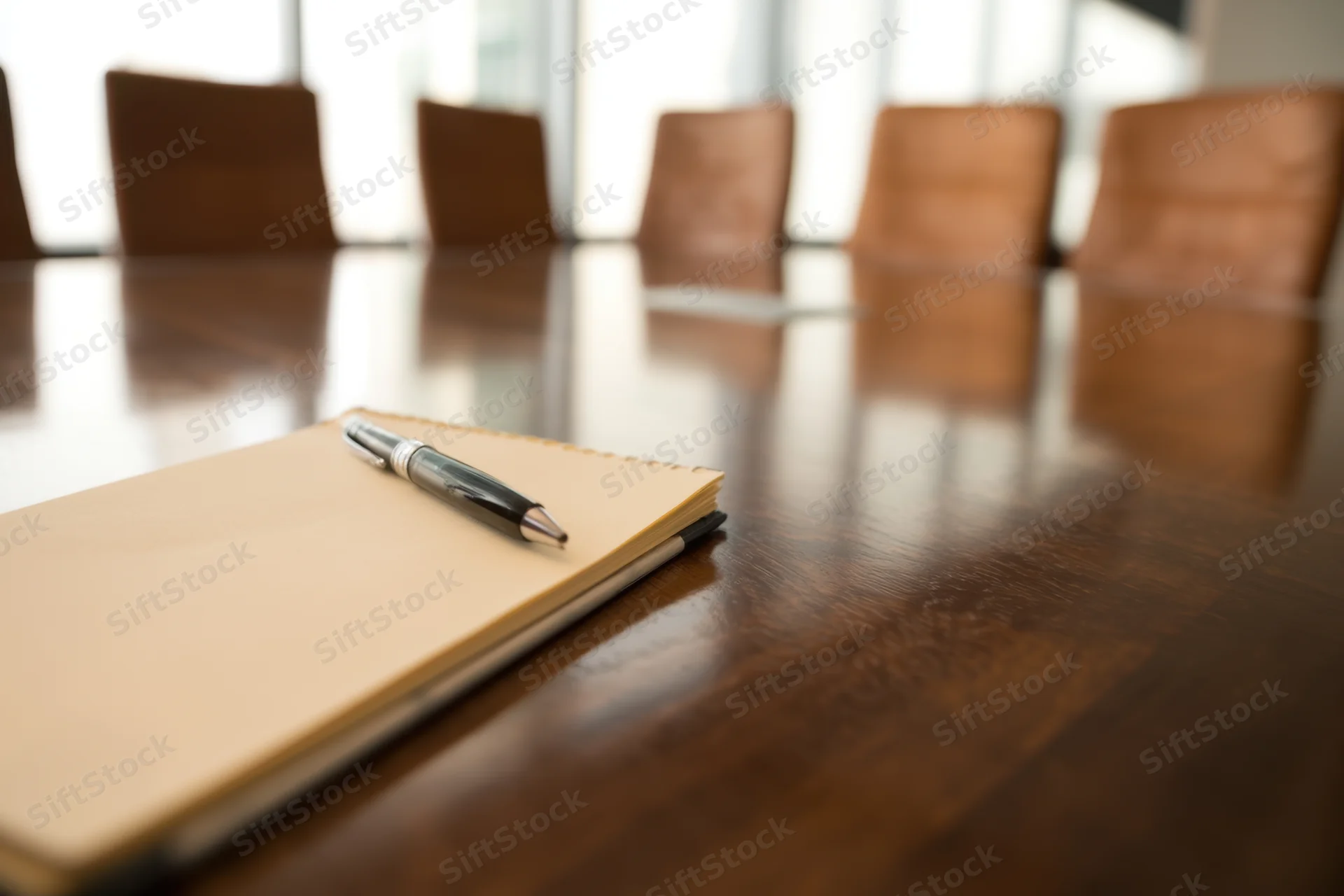 Notebook and pen on a polished wooden conference table with chairs in the background