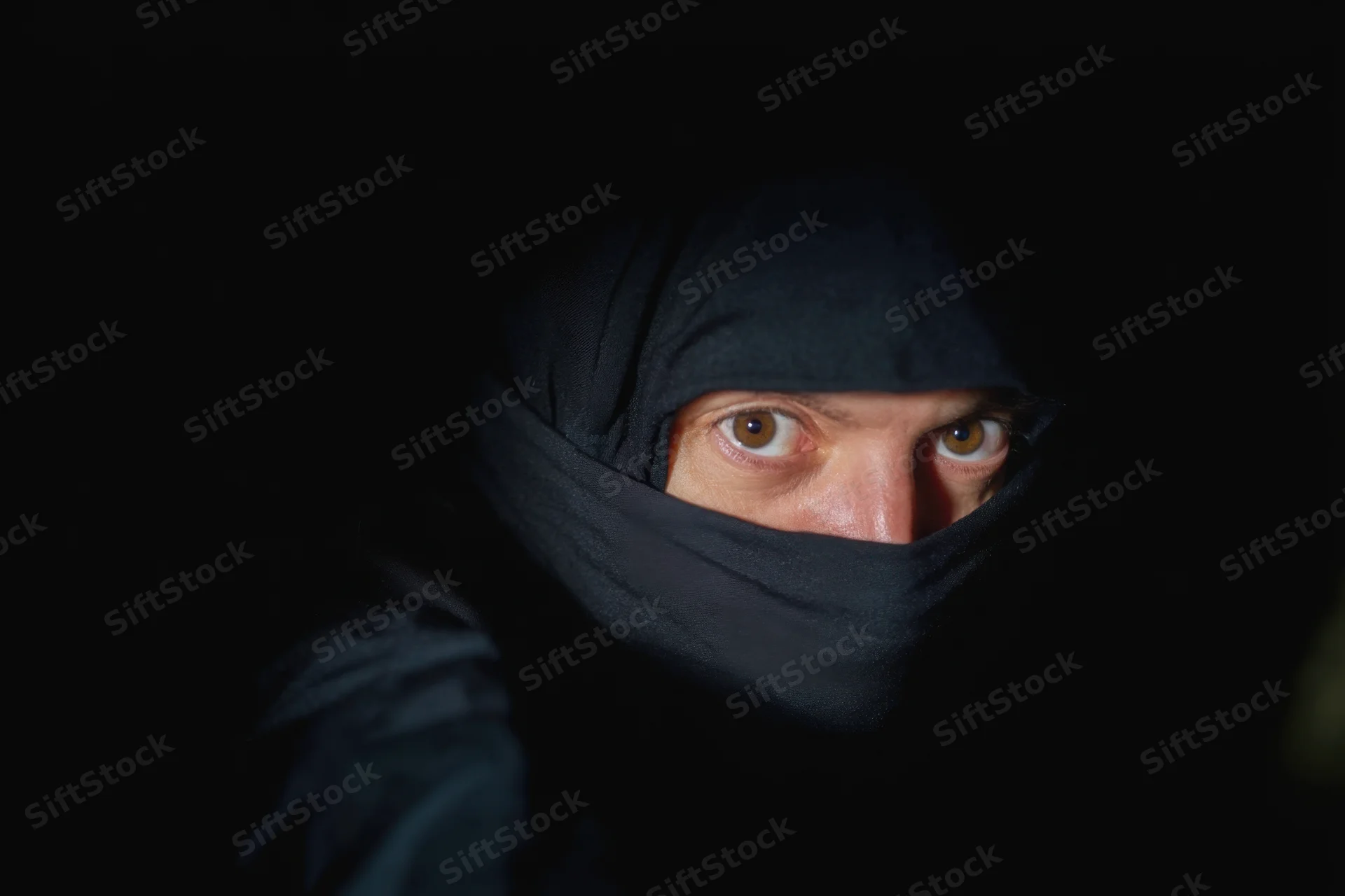 Hooded ninja with intense eyes staring from darkness