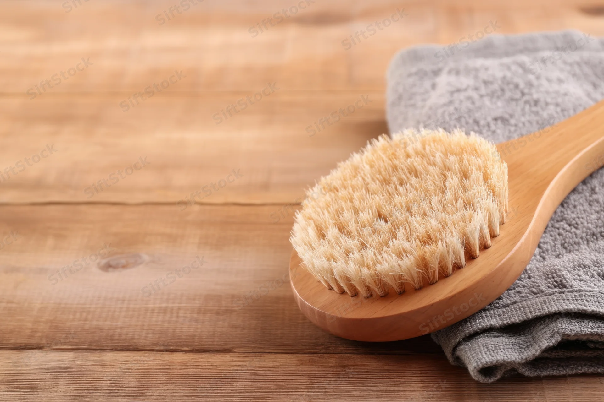 Wooden bath brush with soft bristles resting on a folded gray towel on a wooden surface