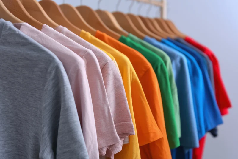 Colorful t-shirts arranged in a row on wooden hangers on a rack