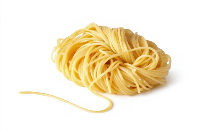 Mound of cooked spaghetti with one strand extending outward on white background