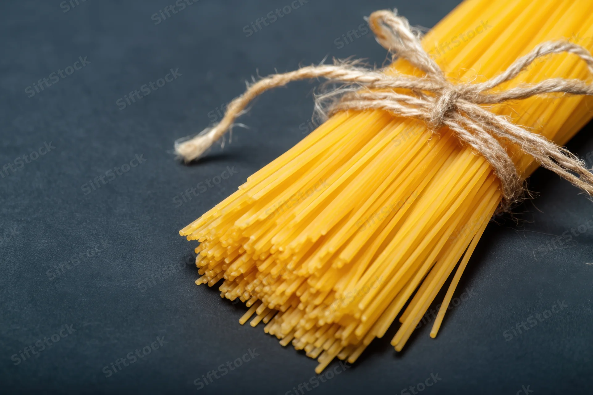 Bundle of uncooked yellow spaghetti tied with twine on dark surface