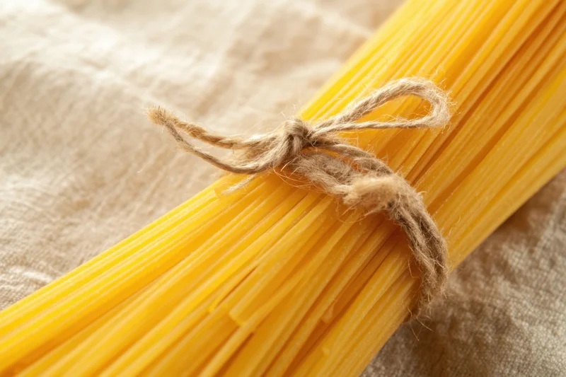 Bundle of uncooked yellow spaghetti tied with twine on a beige cloth surface