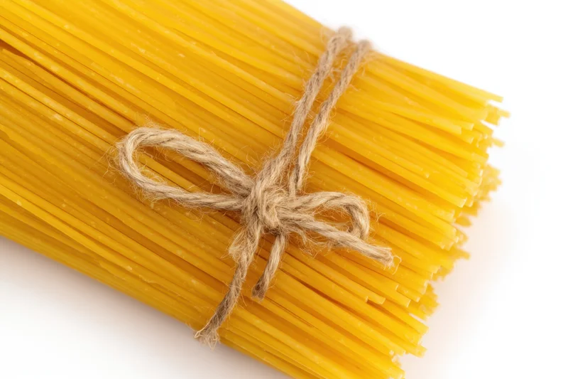 Bundle of uncooked yellow spaghetti tied with twine on white background