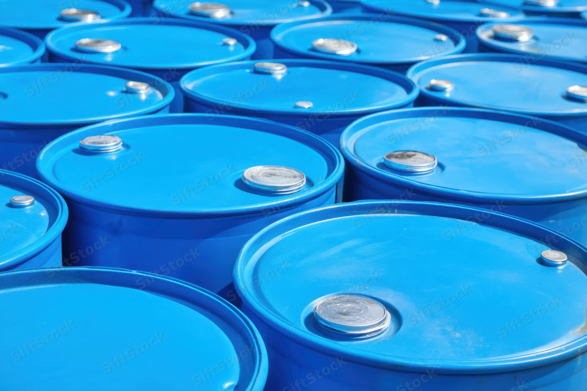 Bright blue metal barrels stacked in neat rows outdoors in a storage facility