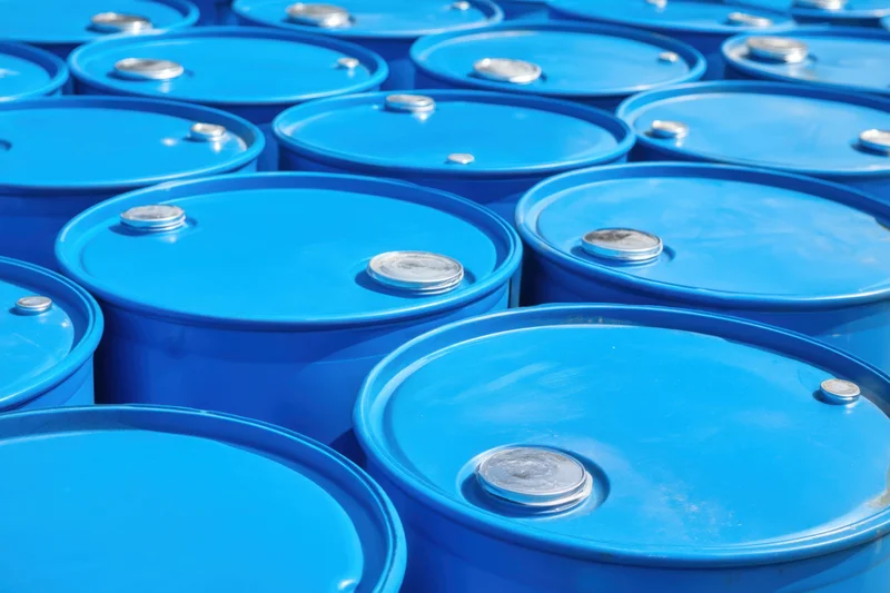 Bright blue metal barrels stacked in neat rows outdoors in a storage facility