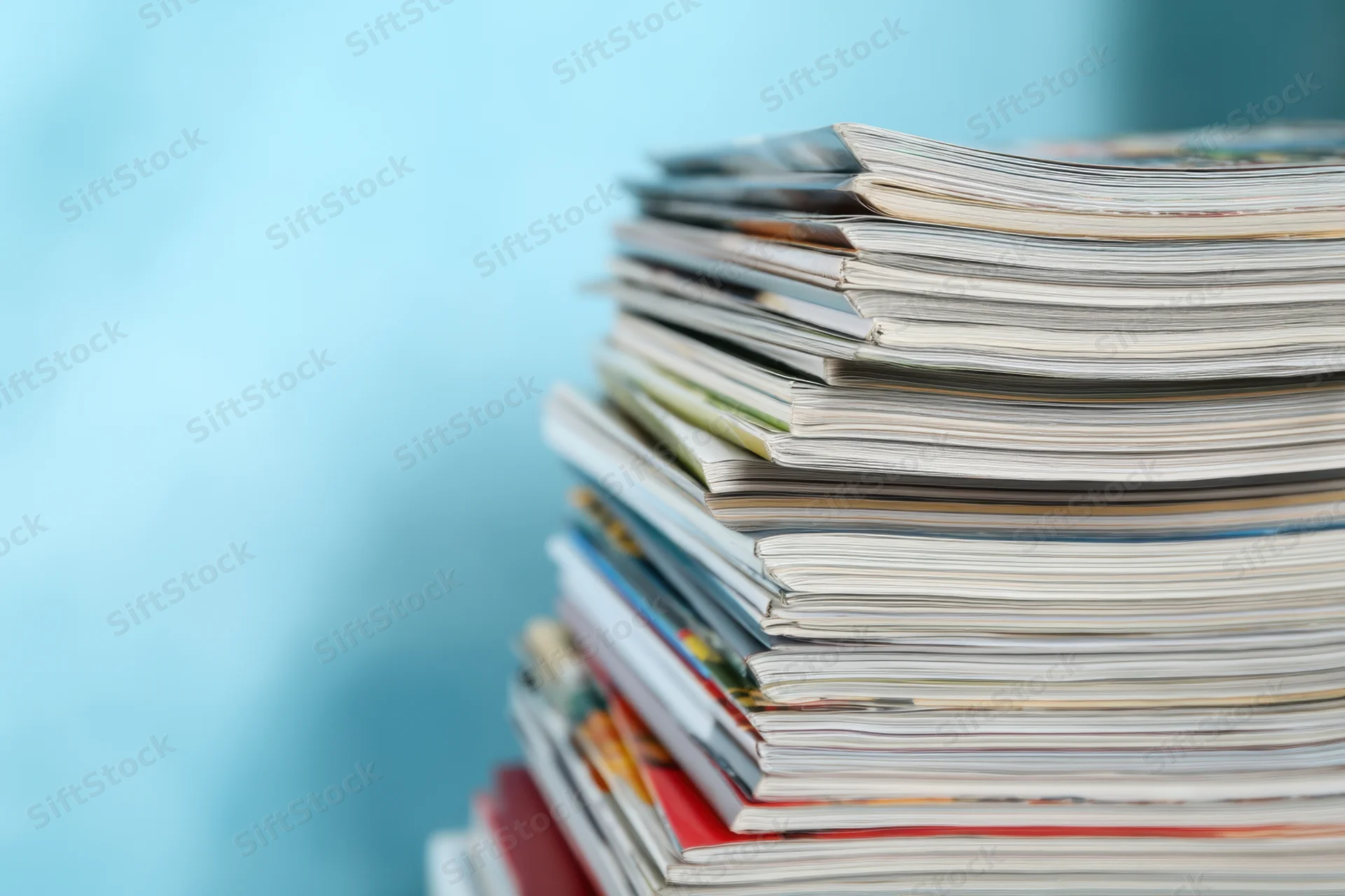 Stack of magazines arranged vertically against a light blue background with copyspace on the left