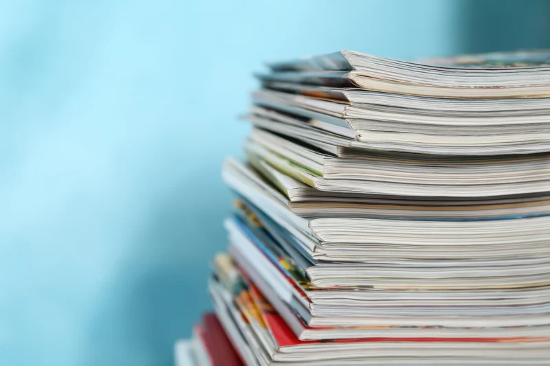 Stack of magazines arranged vertically against a light blue background with copyspace on the left