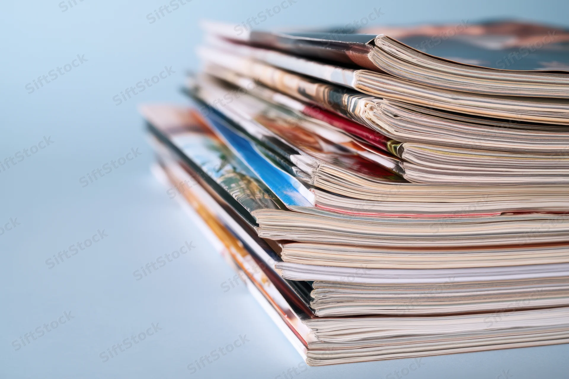 Stack of magazines arranged neatly on a light blue surface with copyspace on the left side