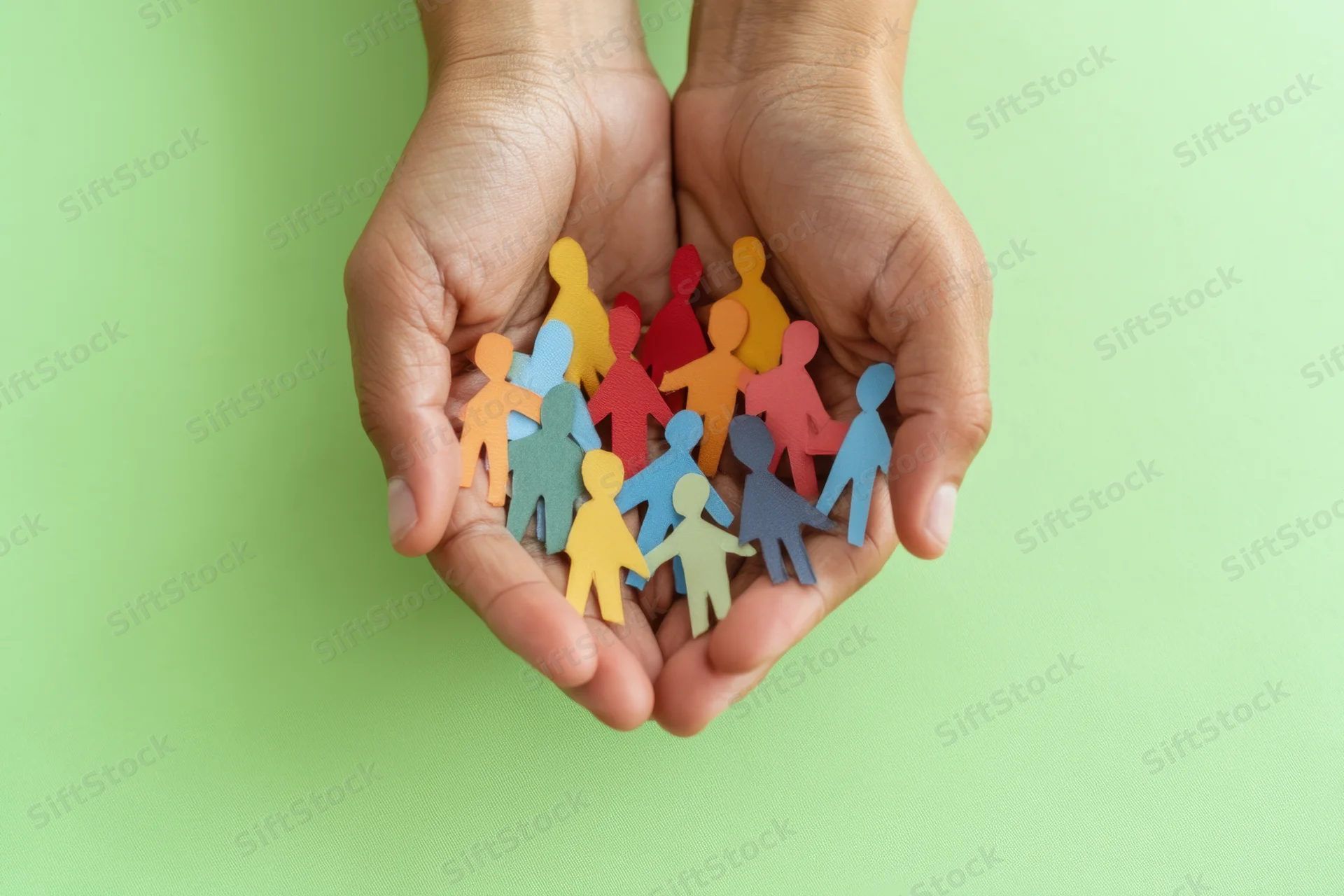 Hands cradling colorful paper cutouts of people against a green background