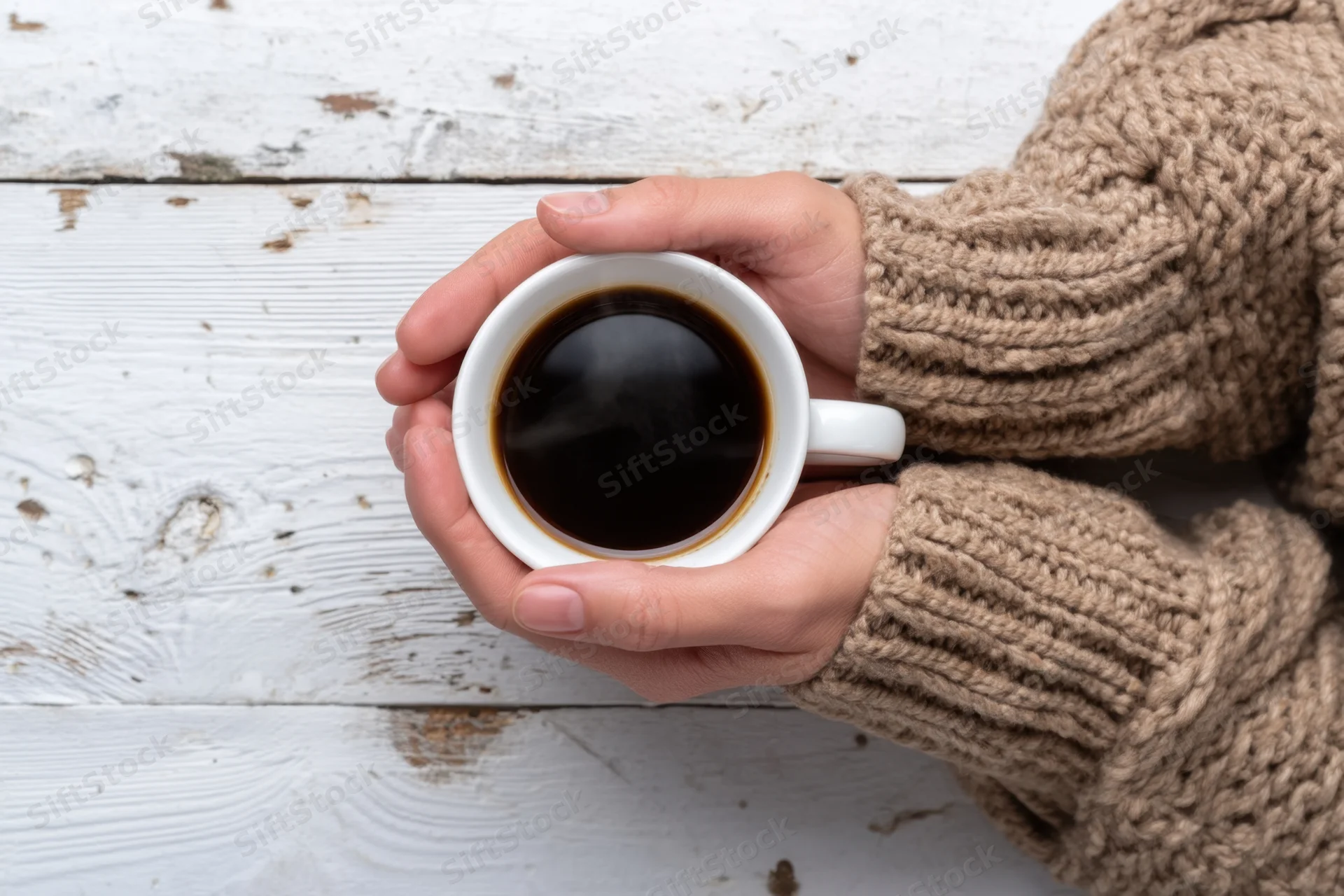Hands holding a steaming cup of black coffee on a white wooden table