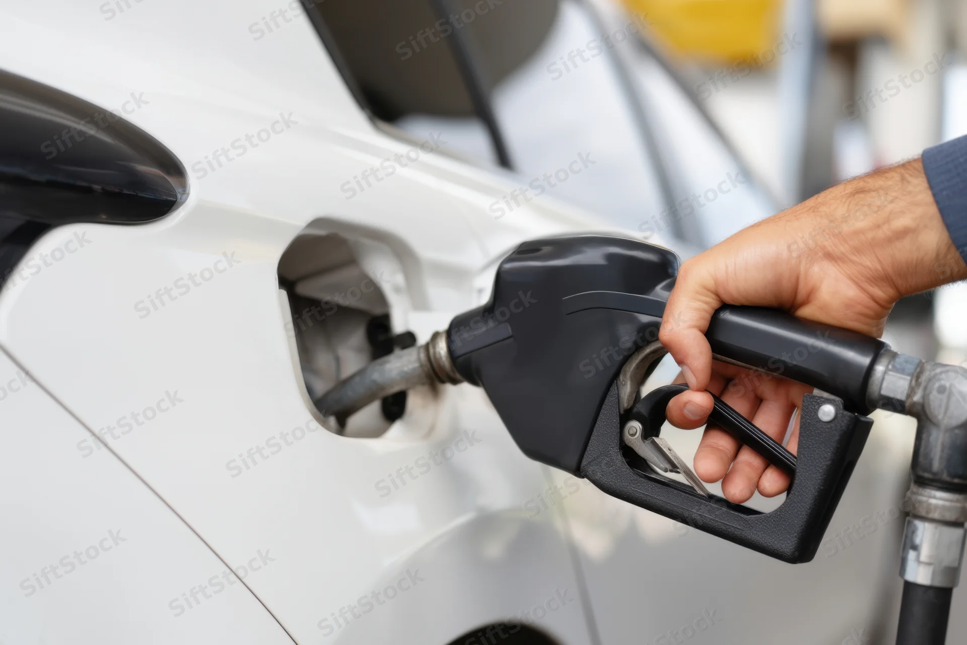 Man refueling a white car at a gas station with a fuel pump nozzle in hand