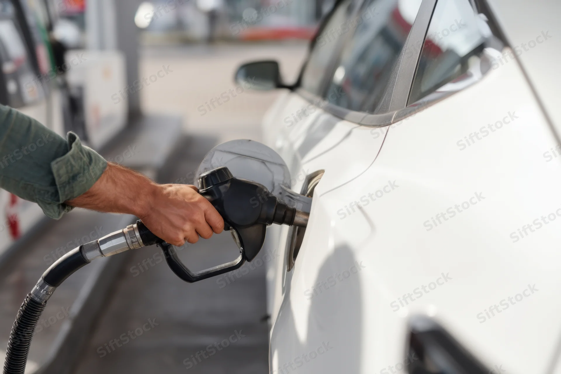 Man refueling a white car at a gas station with a fuel pump nozzle