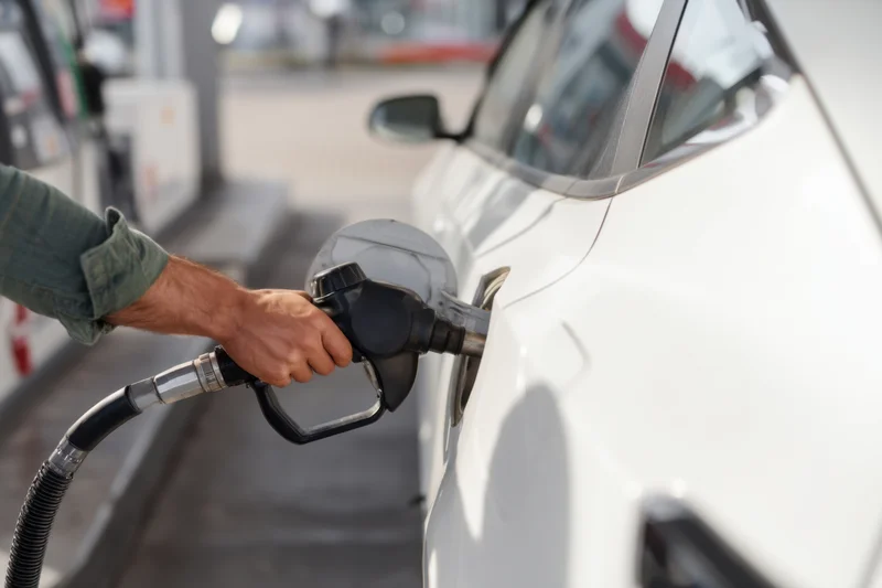 Man refueling a white car at a gas station with a fuel pump nozzle
