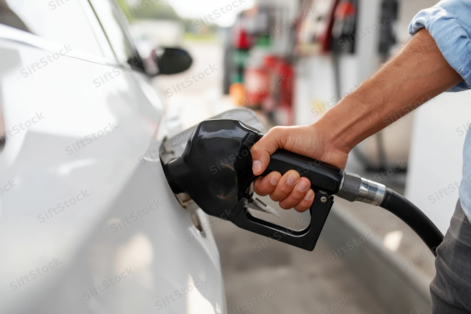 Man refueling a white car at a gas station with a fuel nozzle in hand