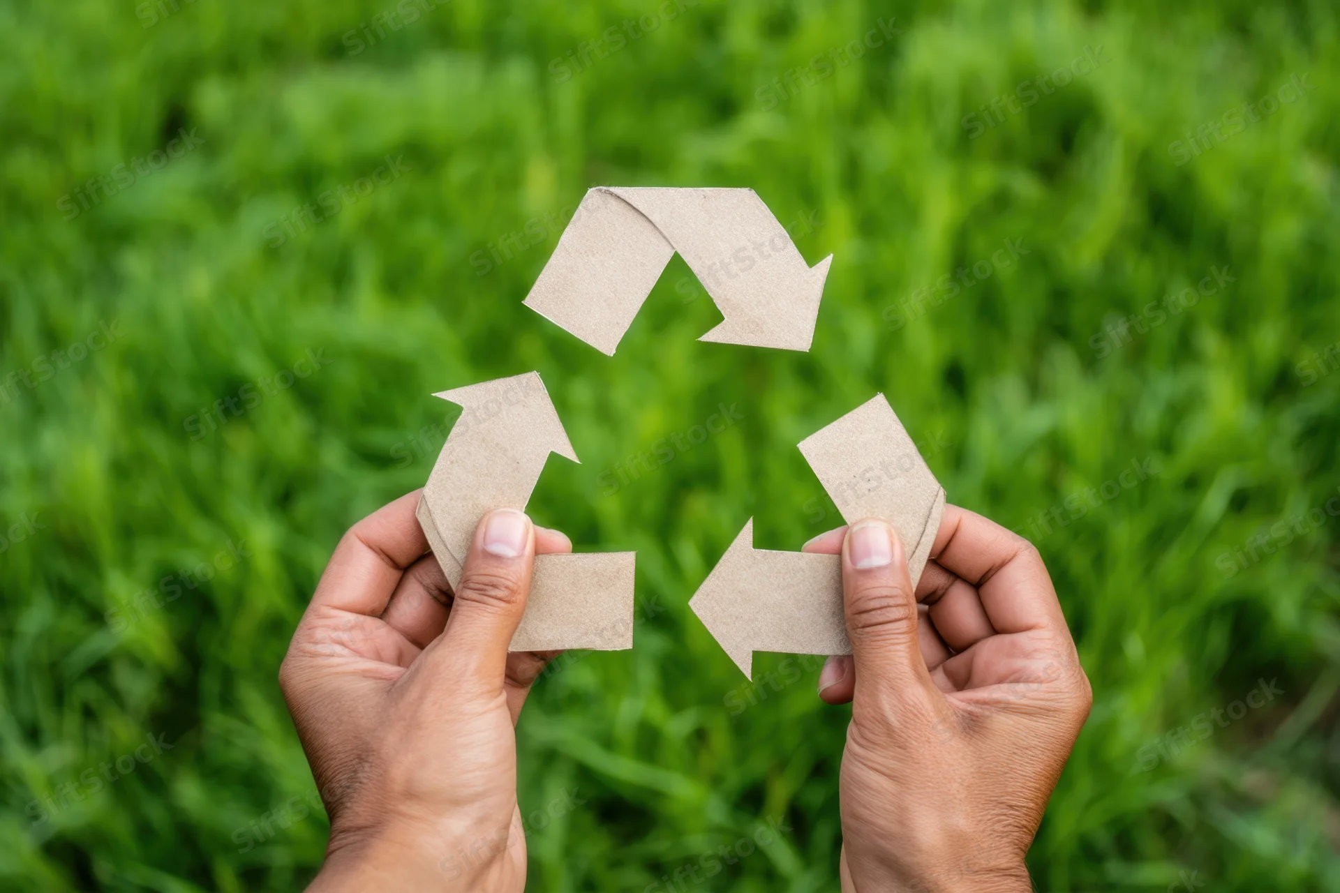 Hands holding a paper recycling symbol against a green grass background