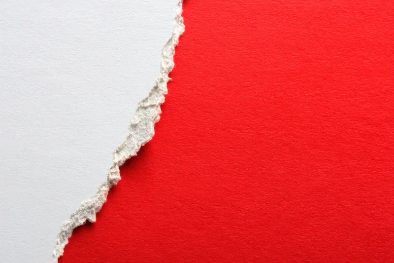 Torn white paper revealing red surface with textured edge