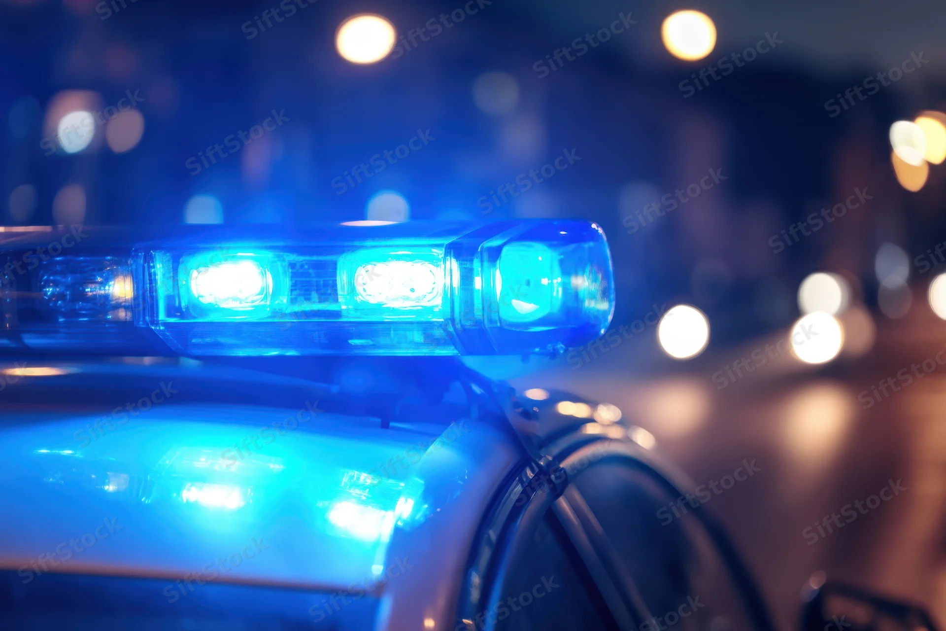 Close-up of flashing blue police car light on rooftop at night on wet city street
