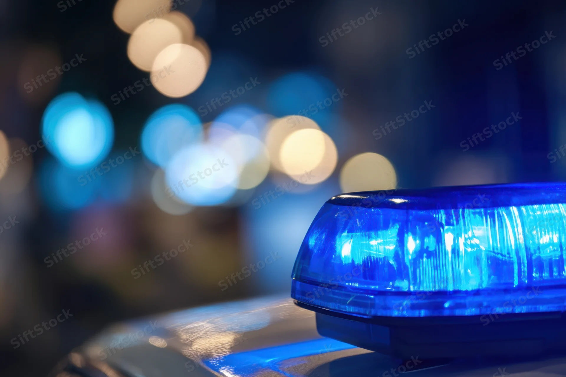 Close-up of a flashing blue police light on a patrol car at night with blurred city lights in the background