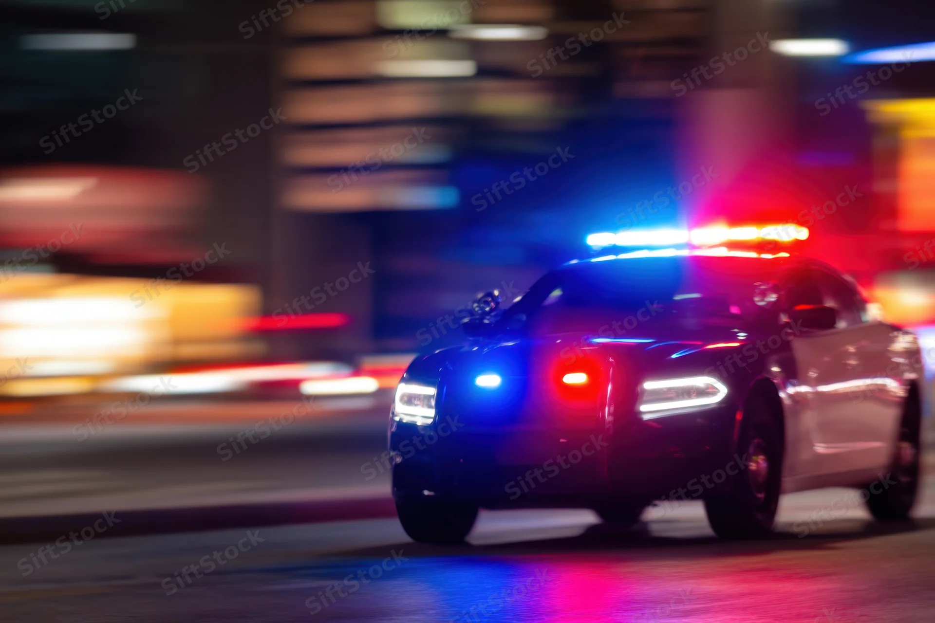 Police car with flashing blue and red lights moving at speed on a city street at night