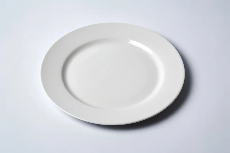 White ceramic plate resting on plain surface with soft shadow and reflection