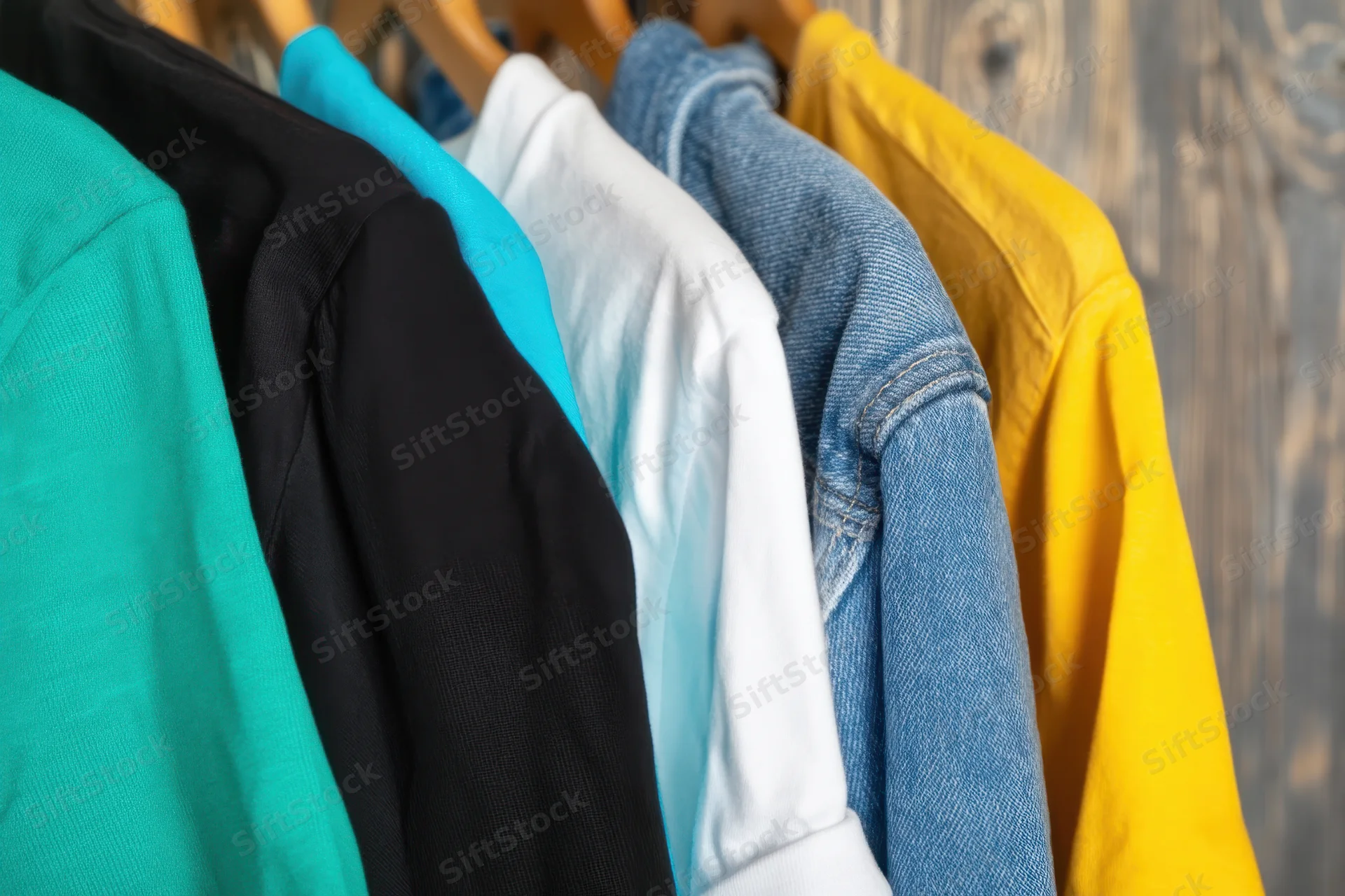 Row of colorful t-shirts hanging on wooden hangers against a wood background