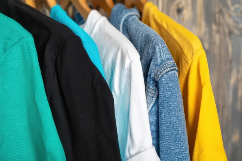 Row of colorful t-shirts hanging on wooden hangers against a wood background