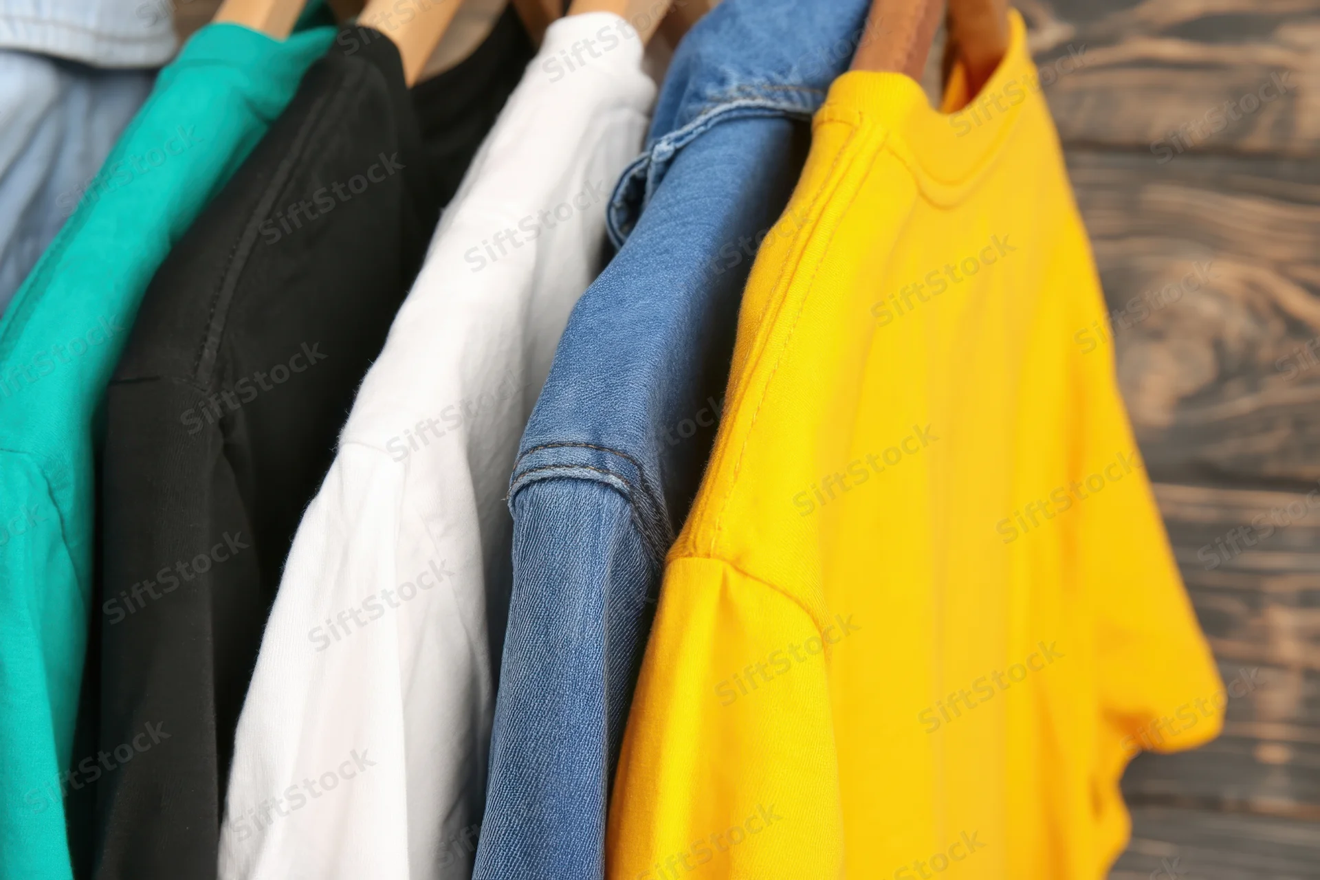 Row of colorful t-shirts hanging on wooden hangers against a rustic wood background