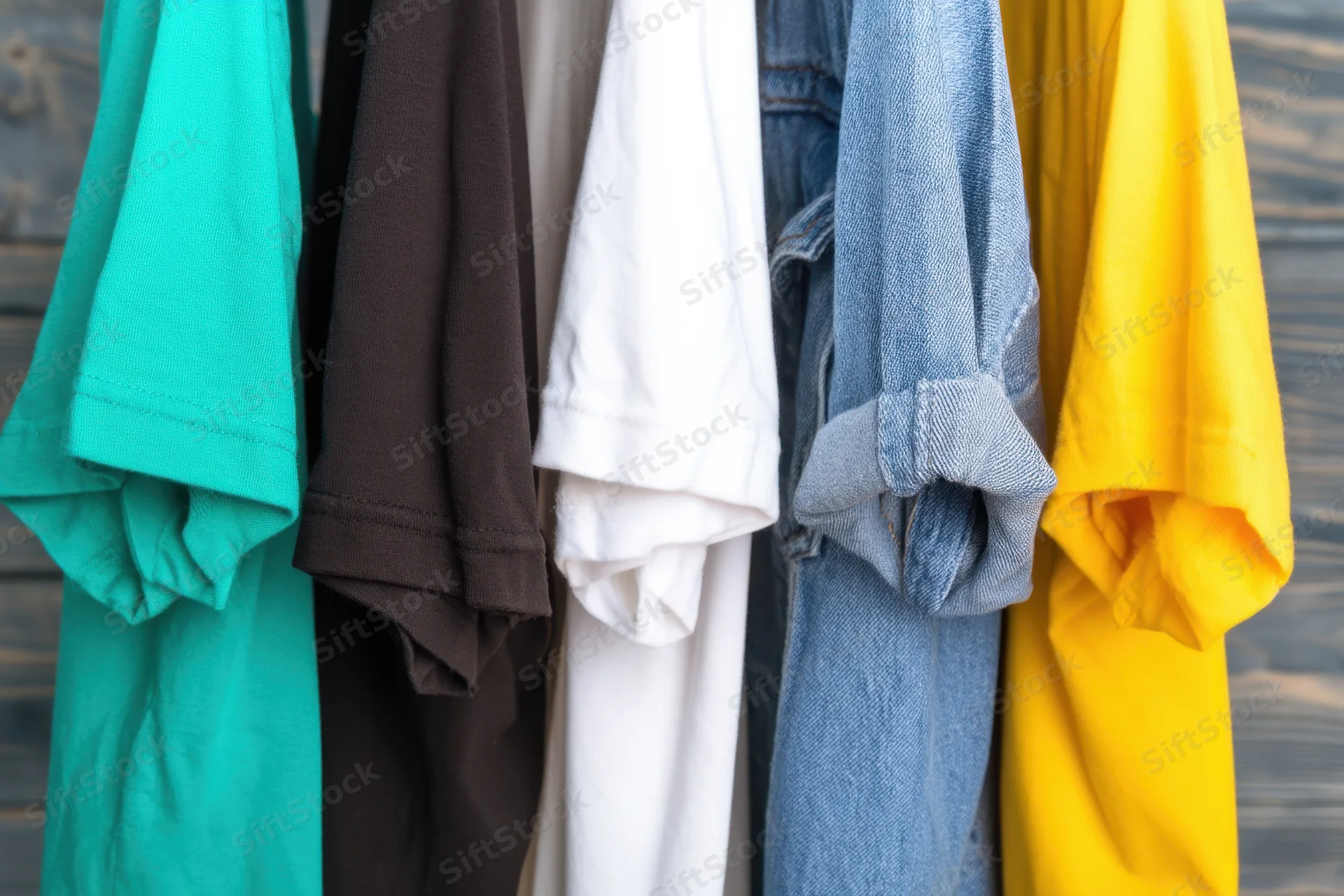 Row of hanging t-shirts in various colors including teal and denim against a wooden background