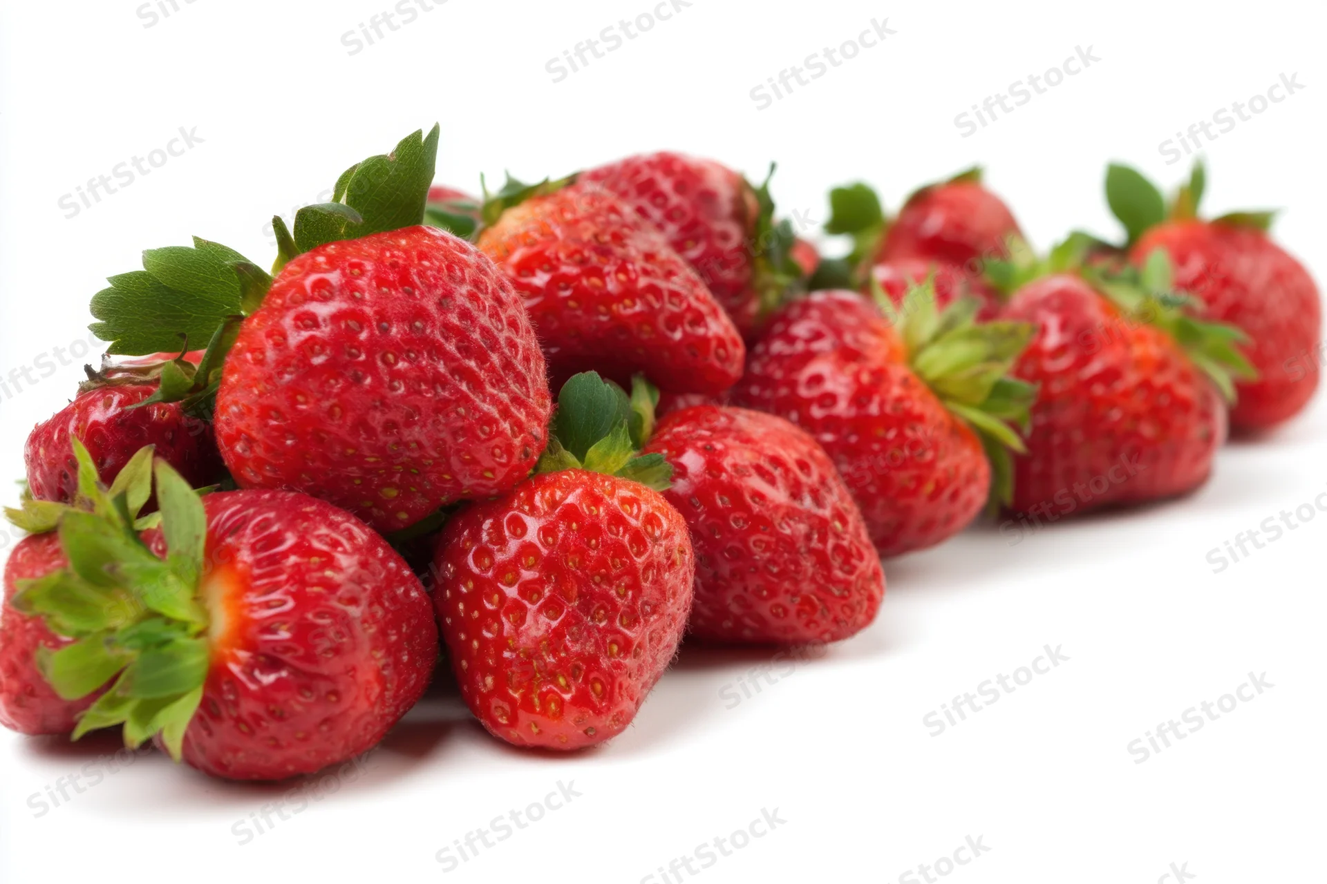 Row of ripe strawberries arranged on white background with green stems and leaves