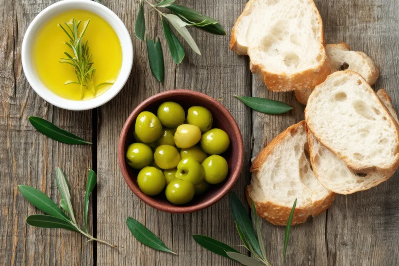Green olives and olive oil with bread slices arranged on a rustic wooden table