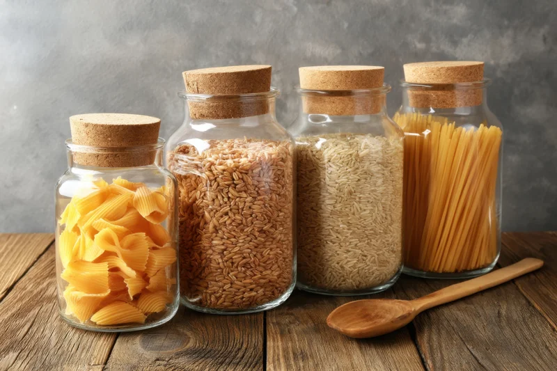 Glass jars filled with uncooked pasta and rice on a rustic wooden table