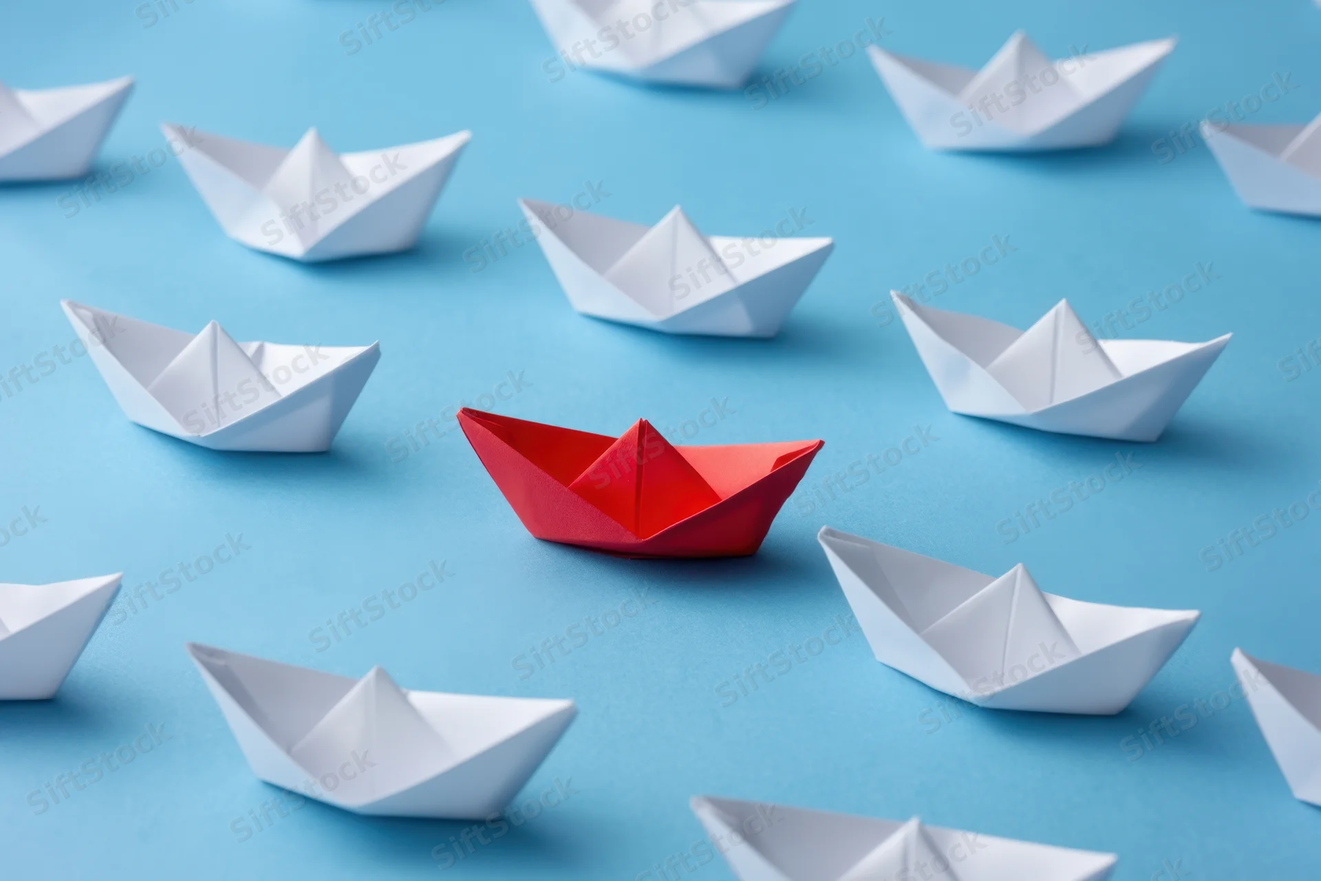 Red paperboat centered among white ones on blue background