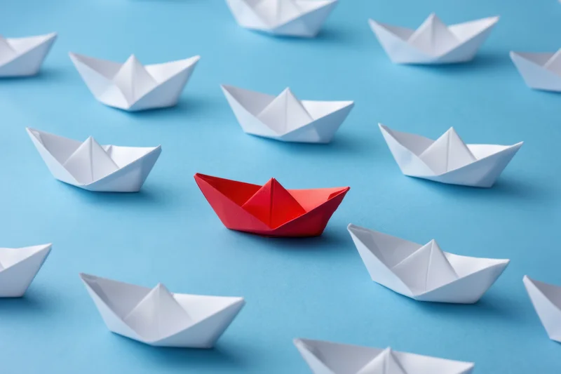 Red paperboat centered among white ones on blue background