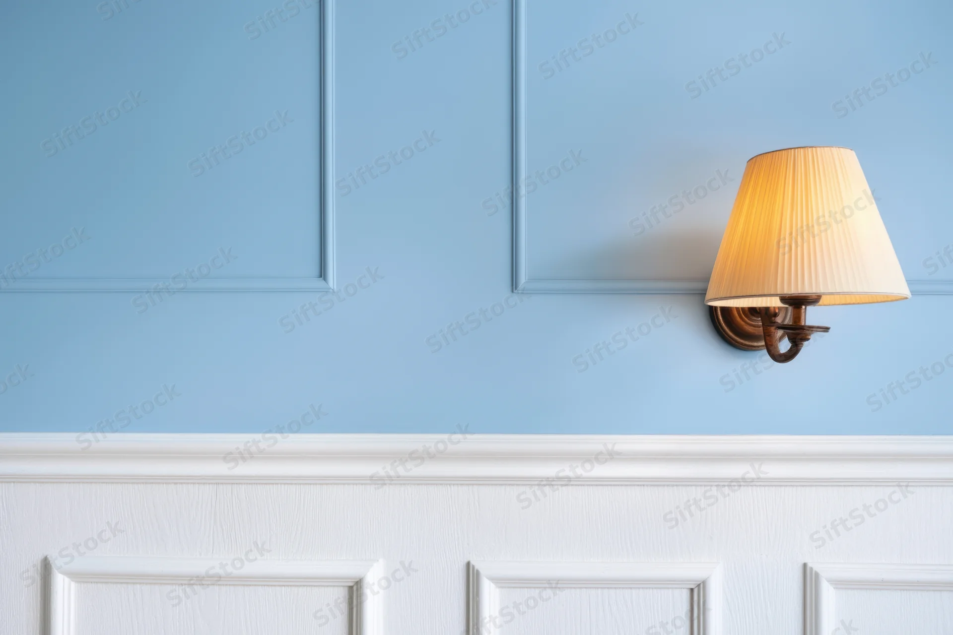 Soft blue paneled wall with white wainscoting and brass sconce light fixture
