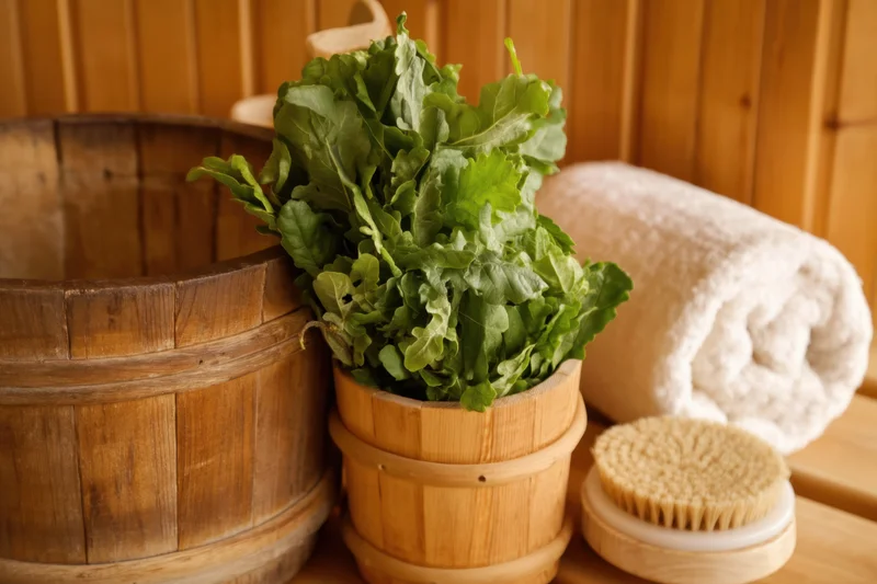 Fresh arugula in a wooden bucket beside a towel and brush in a sauna with wooden walls
