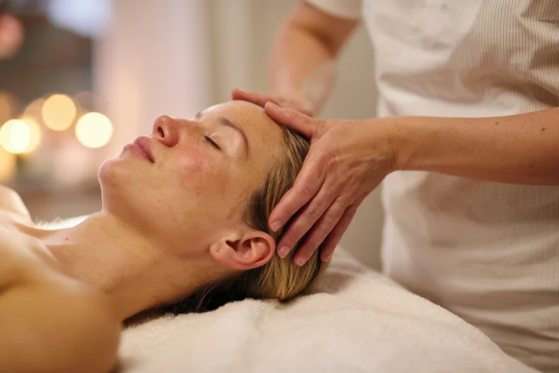 Woman receiving head massage on spa bed with soft lighting and towel under her neck