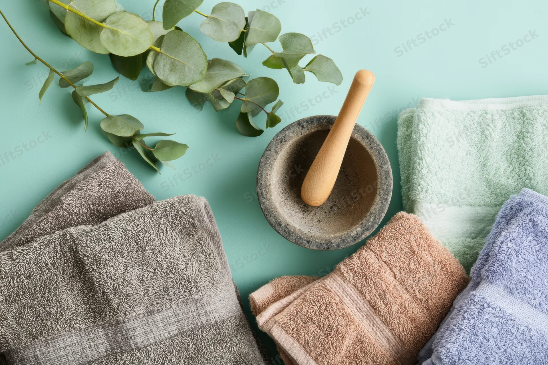 Folded towels and eucalyptus with mortar and pestle arranged on teal background