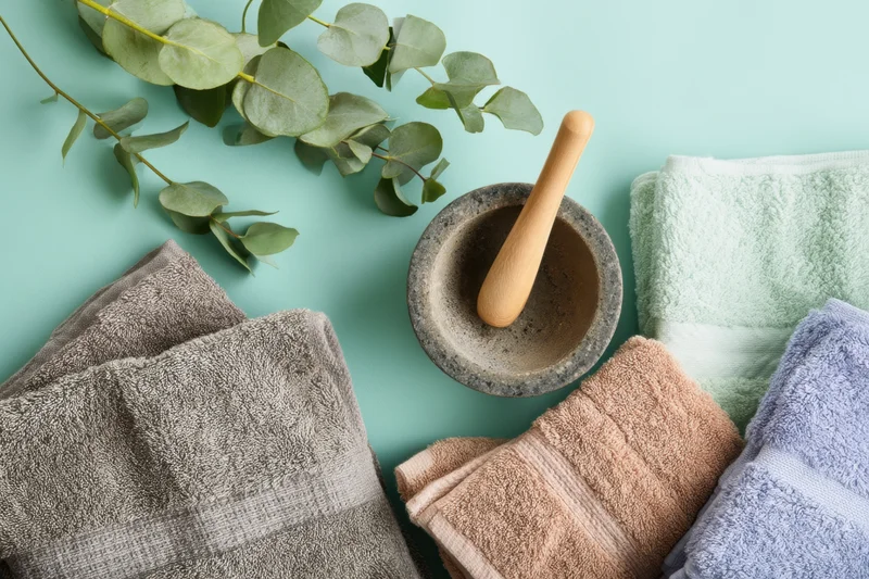 Folded towels and eucalyptus with mortar and pestle arranged on teal background