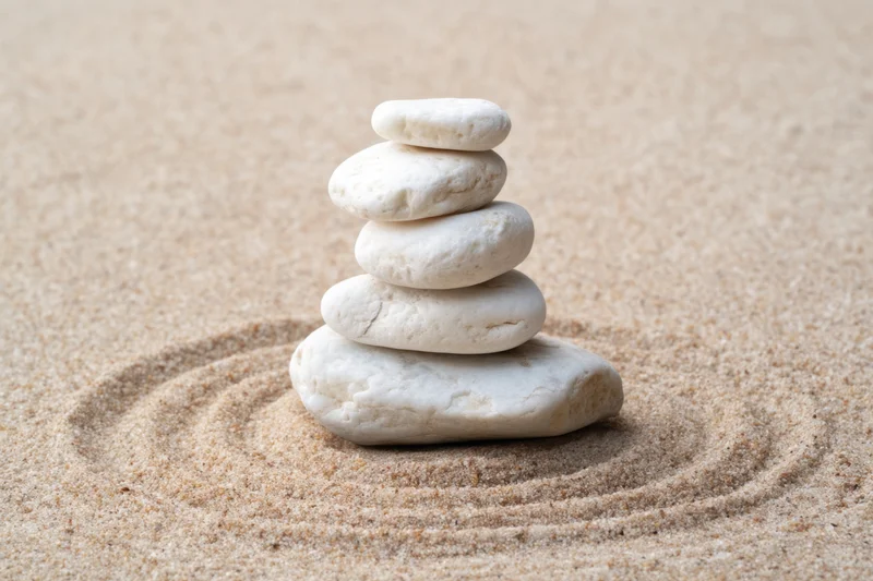 White pebbles stacked in balance on sand with circular ripples around base