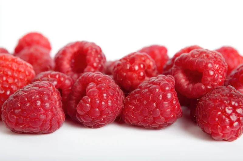 Fresh red raspberries arranged in a row on a white surface