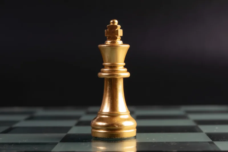 Golden chess king standing on a black and gray checkered board with reflective surface