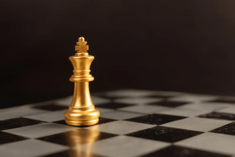 Golden chess king standing on a black and white checkered board