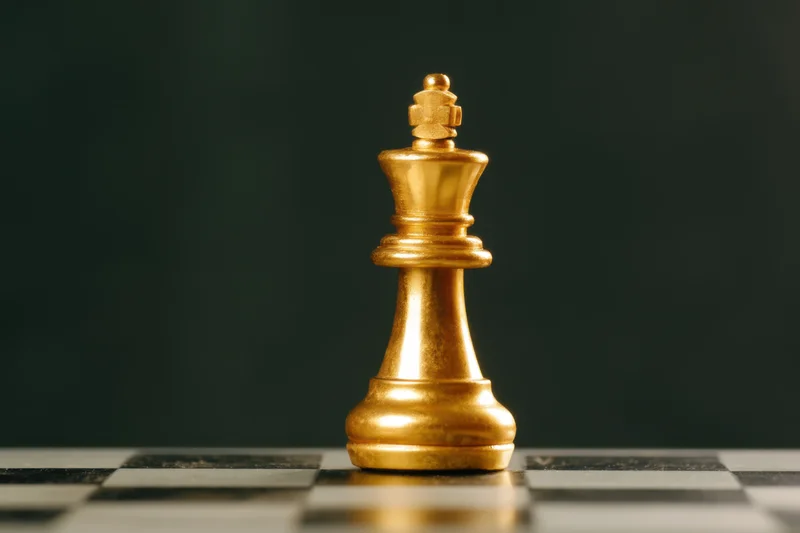 Golden chess king standing on a checkered board against a dark background